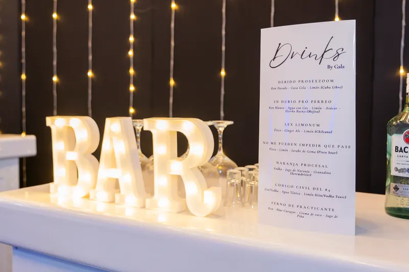 Letras luminosas BAR junto a la carta de cócteles con nombres de la promoción y las copas listas