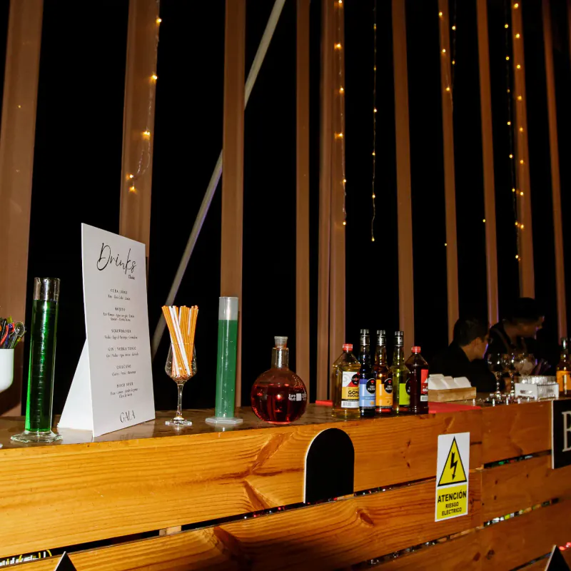 Barra de madera montada con botellas, cristalería y carta de tragos