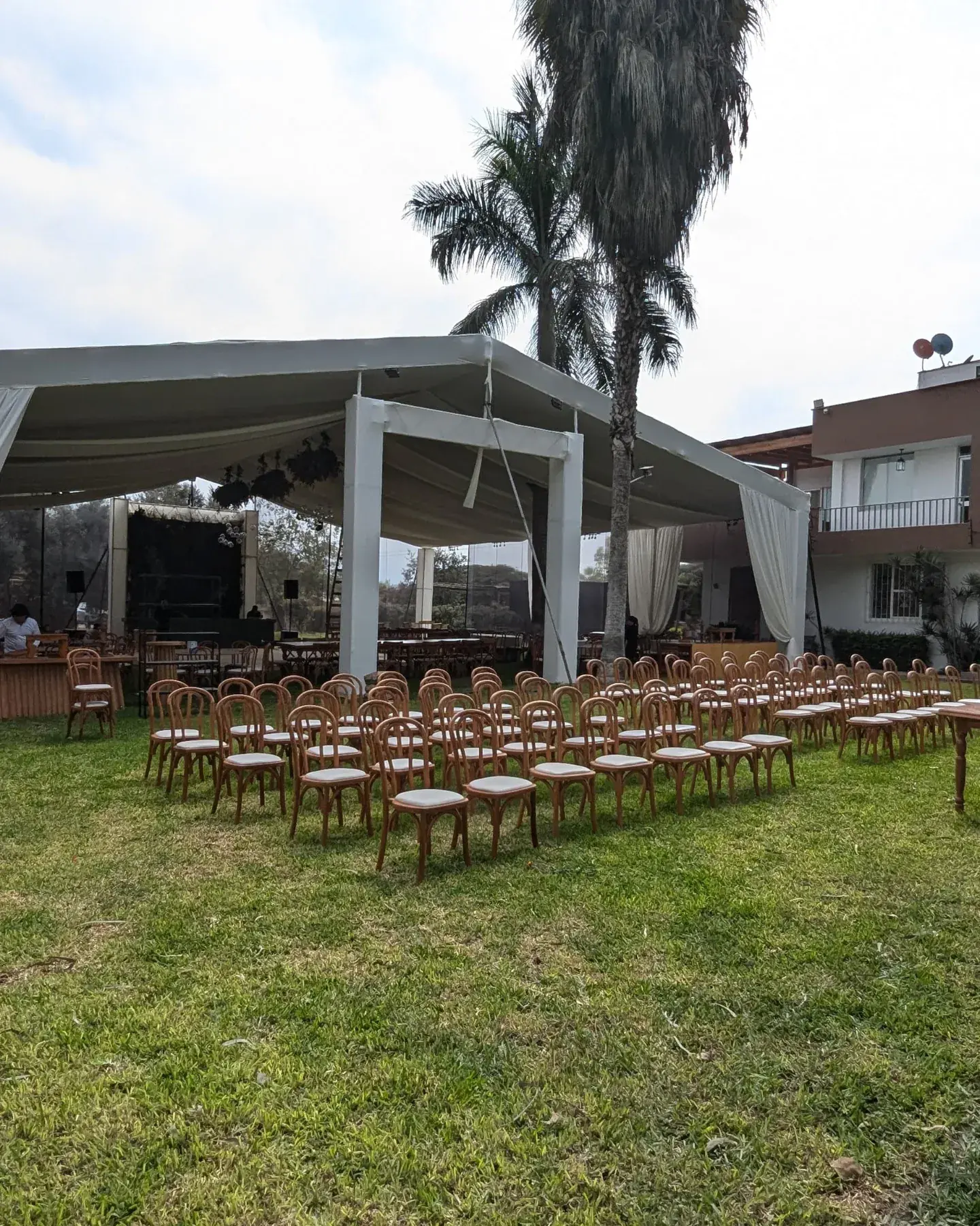 Carpa blanca sobre el jardín con hileras de sillas de madera listas para una ceremonia