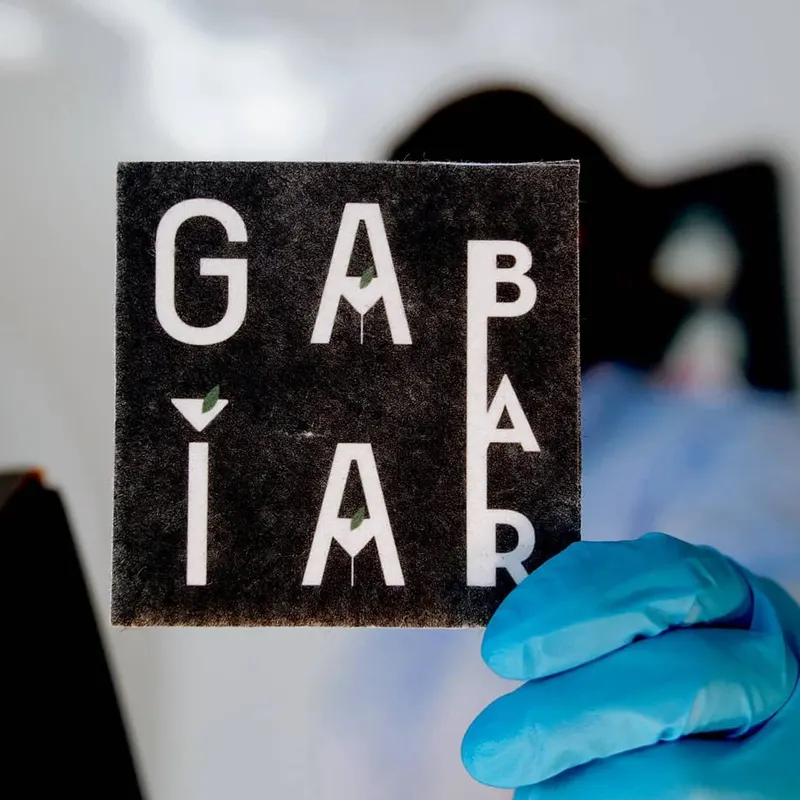 Posavasos de material reciclado con el logo de Gaia Bar, sostenido con un guante azul