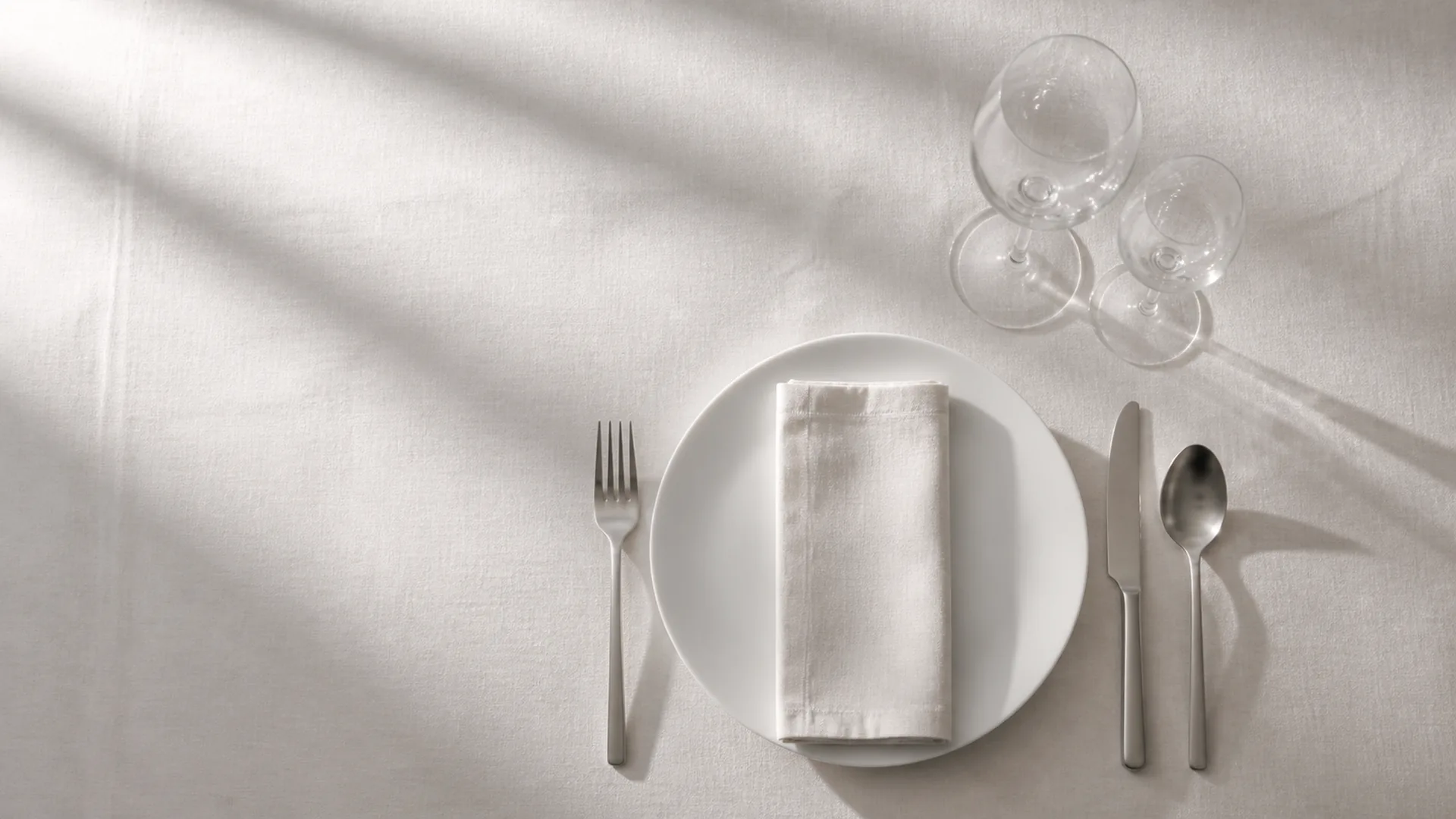 Mesa de banquete vacía con mantel de lino, cristalería y cubertería, vista cenital