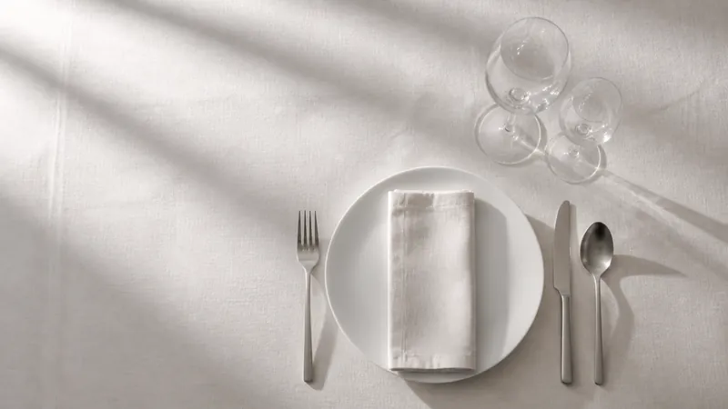 Mesa de banquete vacía con mantel de lino, cristalería y cubertería, vista cenital