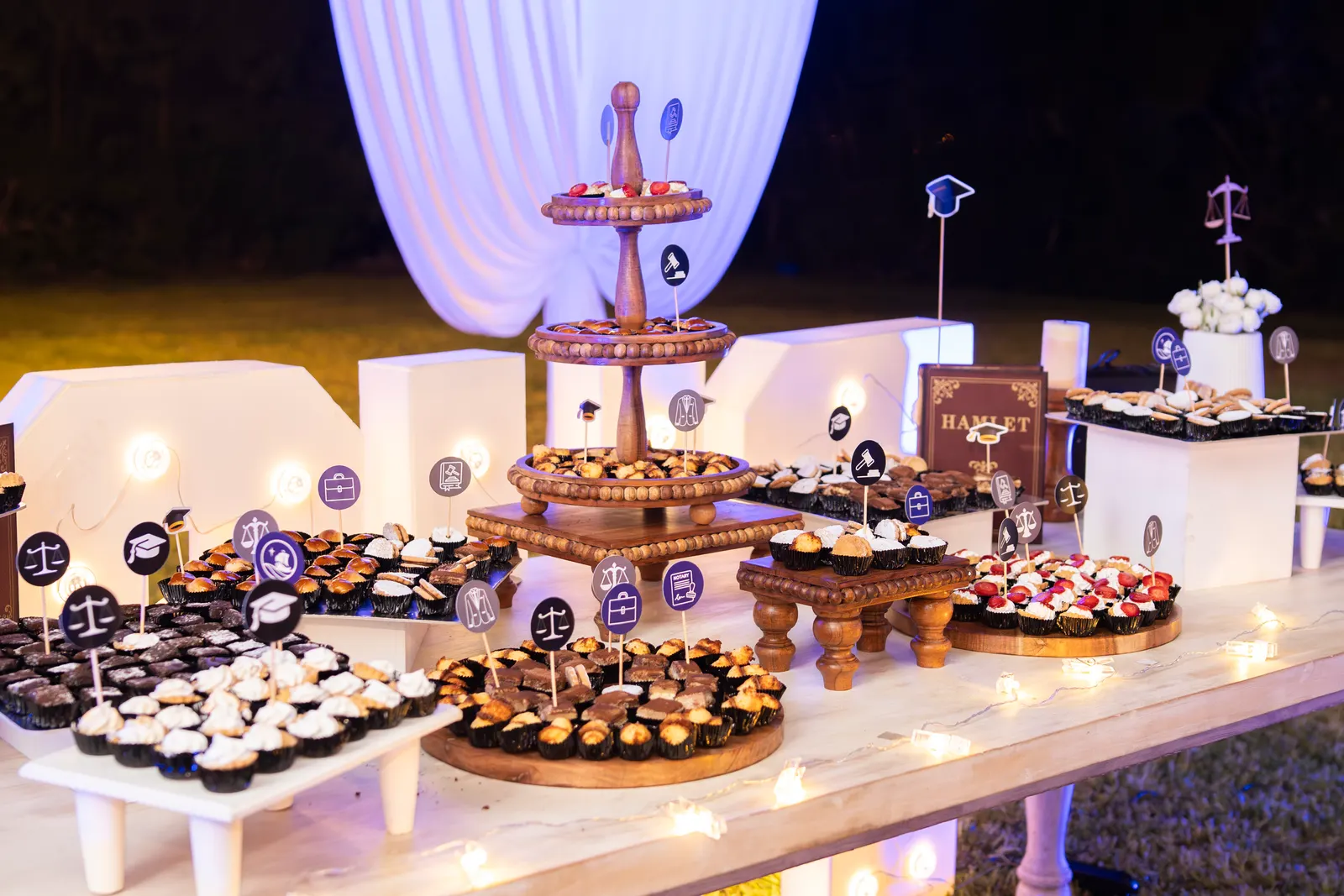 Mesa de postres en bases de madera con banderines de balanzas y birretes, temática de la promoción de Derecho
