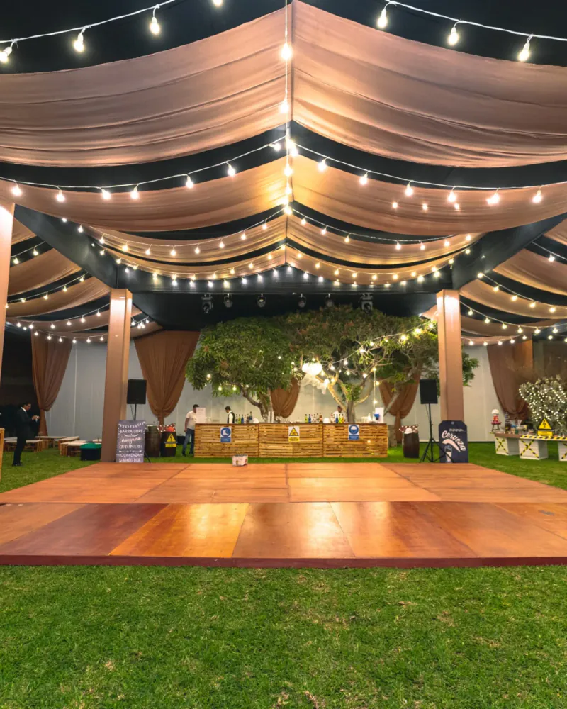 Pista de baile de madera bajo carpa con drapeados y árboles iluminados al fondo