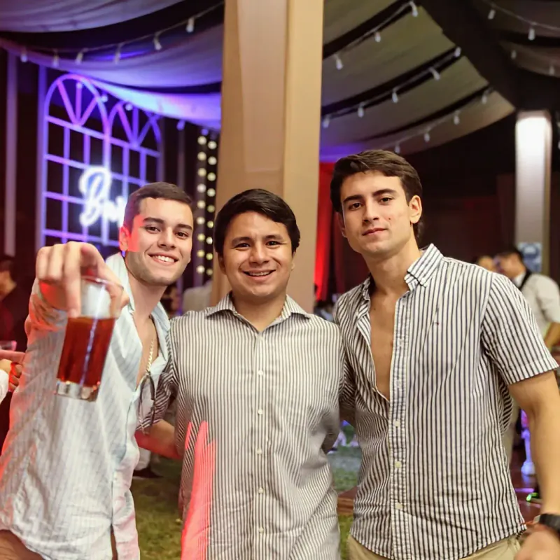 Tres invitados levantando sus tragos en la barra de la fiesta de promoción