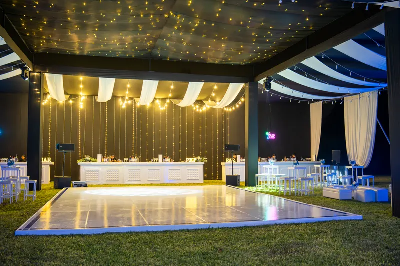 Pista de baile blanca bajo una carpa negra con guirnaldas de luces y la barra al fondo, antes de que lleguen los invitados