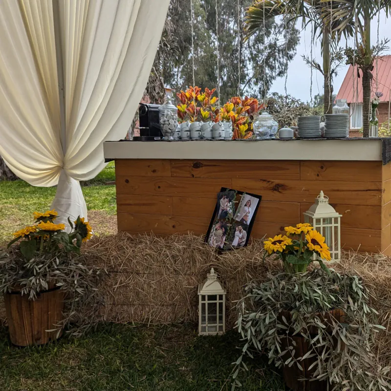 Rincón decorado con fardos de paja, faroles y flores amarillas junto a la carpa